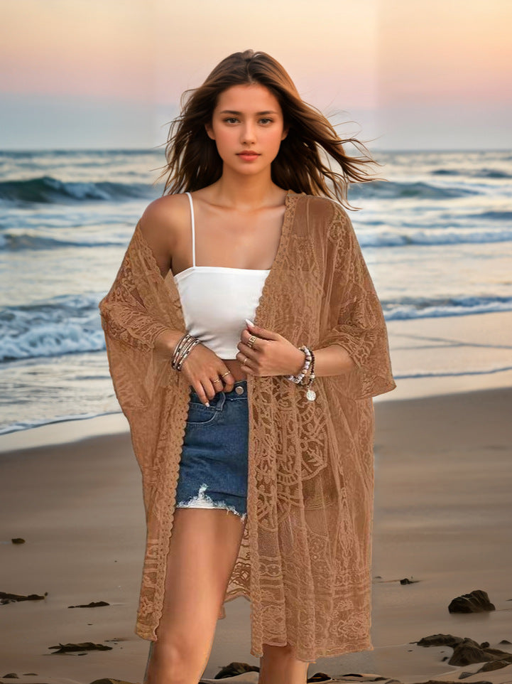 Woman on a beach wearing a beige cover-up, white top, and denim shorts.