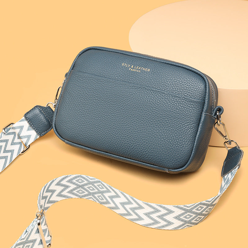 Blue leather crossbody bag with a patterned strap on a beige background