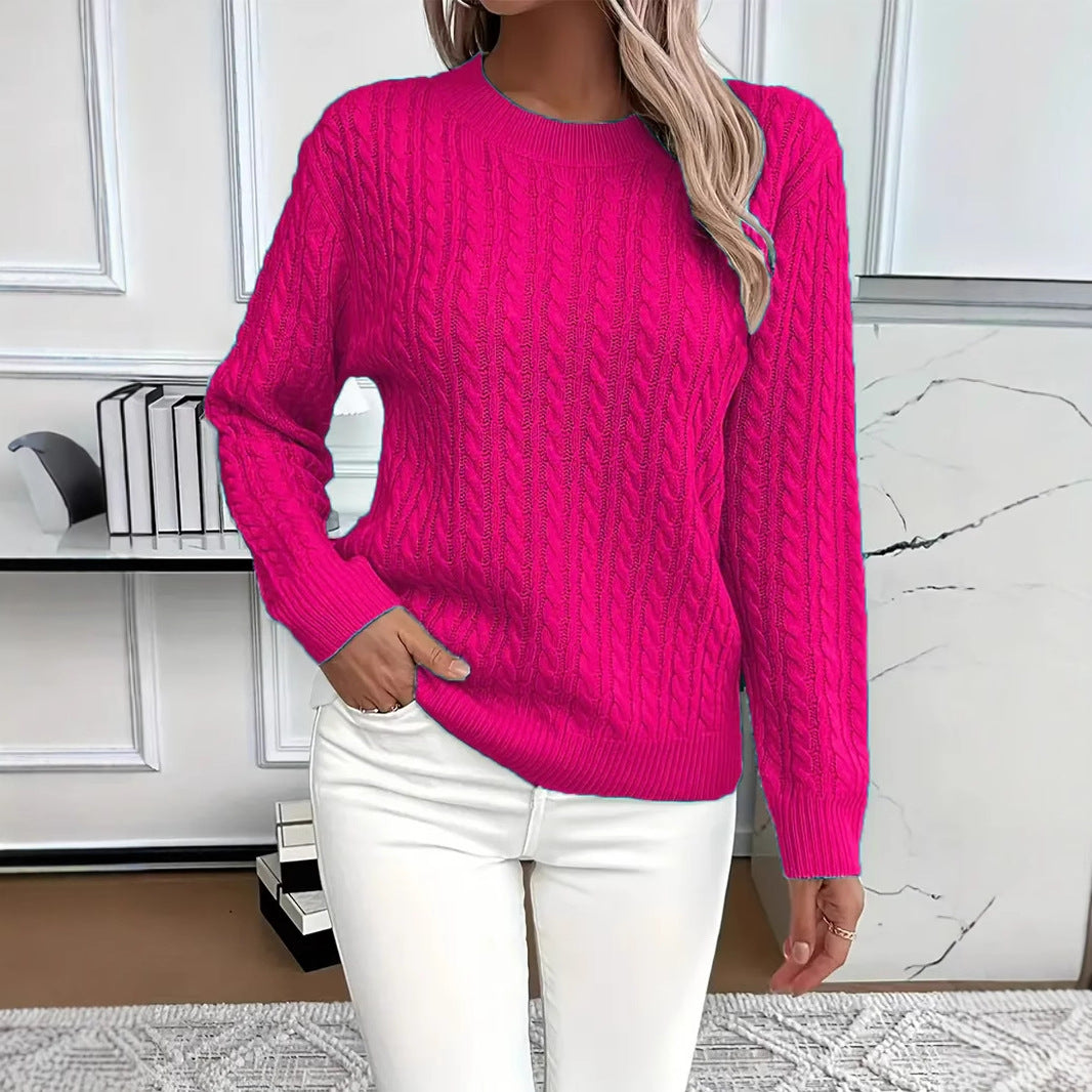 A woman wearing a bright pink cable-knit sweater and white pants, standing in a modern room with white paneled walls and a marble accent.