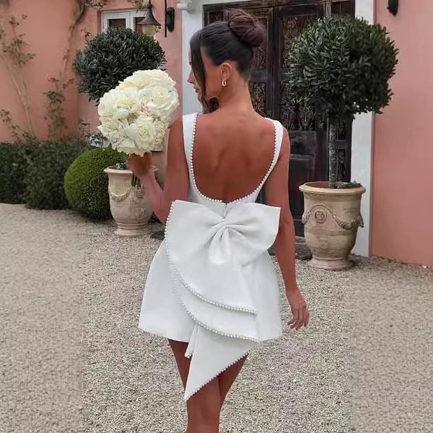 Woman in a white dress with a large bow holding flowers, standing in front of a pink building.