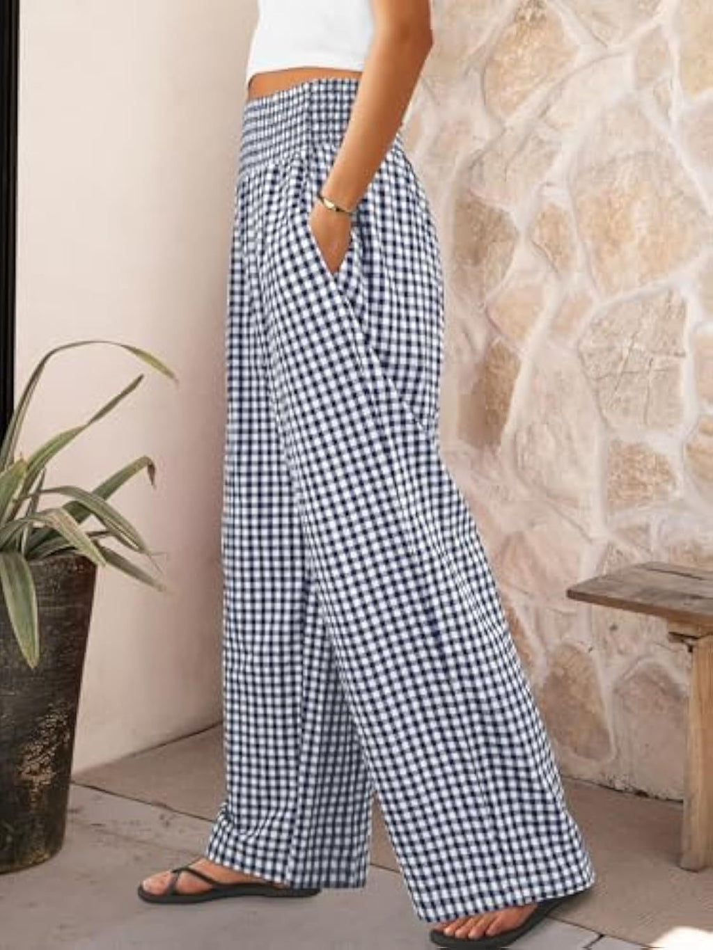 Person wearing blue and white checkered pants standing against a stone wall.
