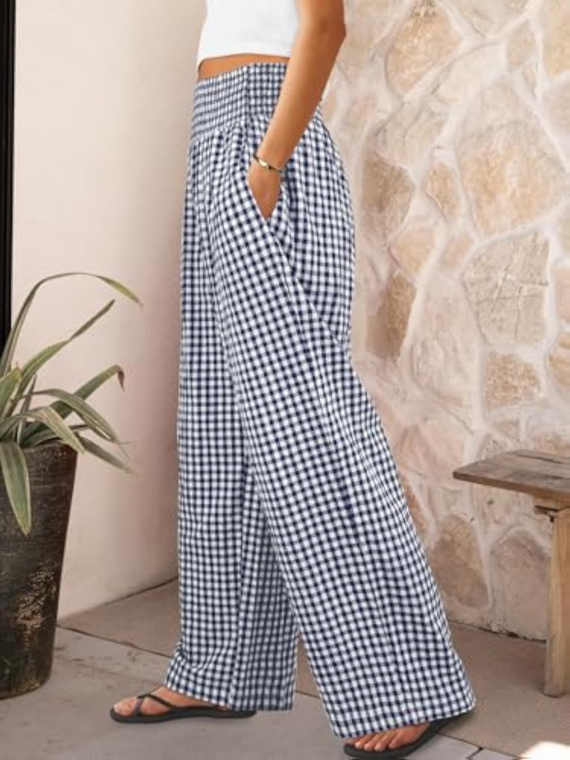 Person wearing blue and white checkered pants standing against a stone wall.
