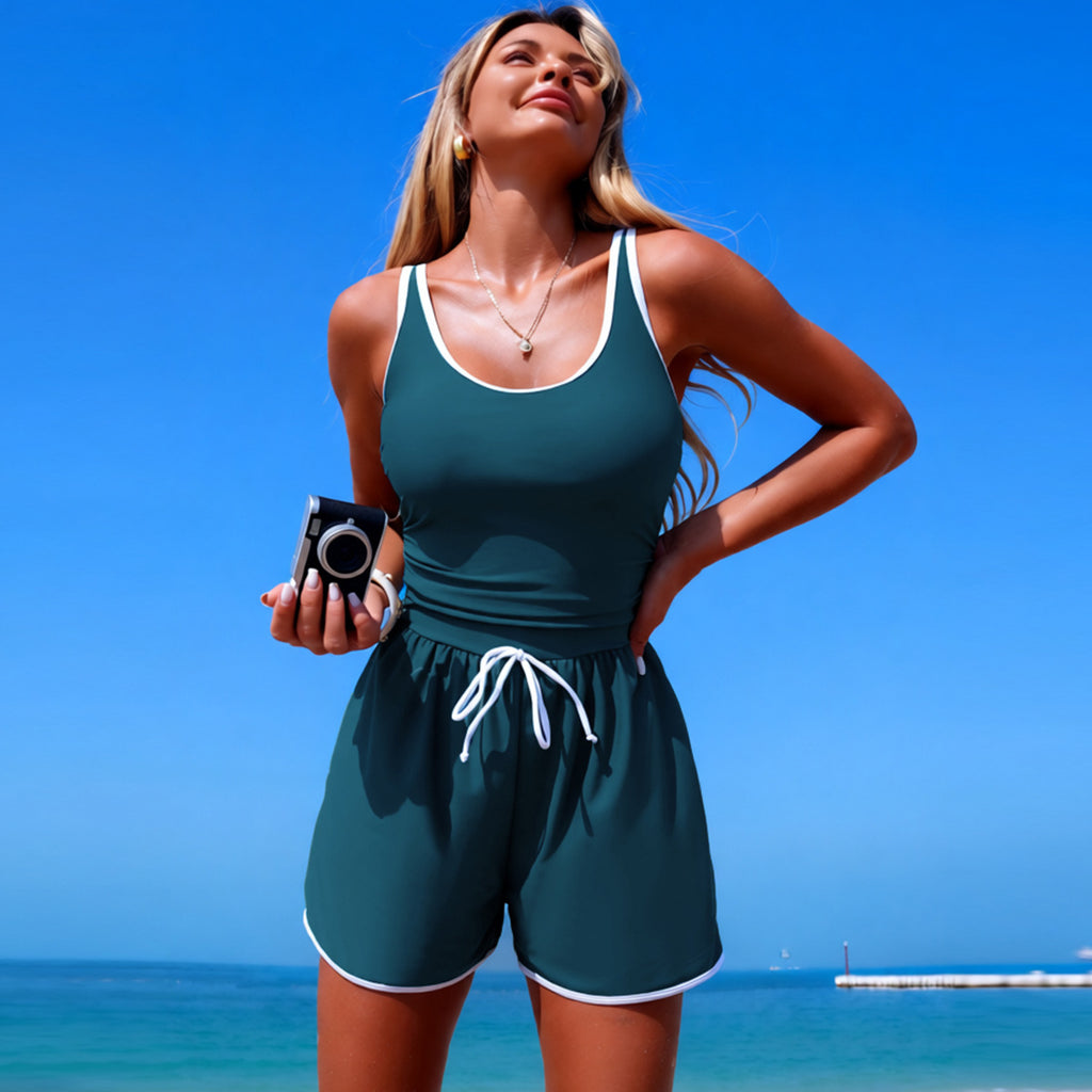 Woman in a green swimsuit holding a camera on a beach with clear blue sky