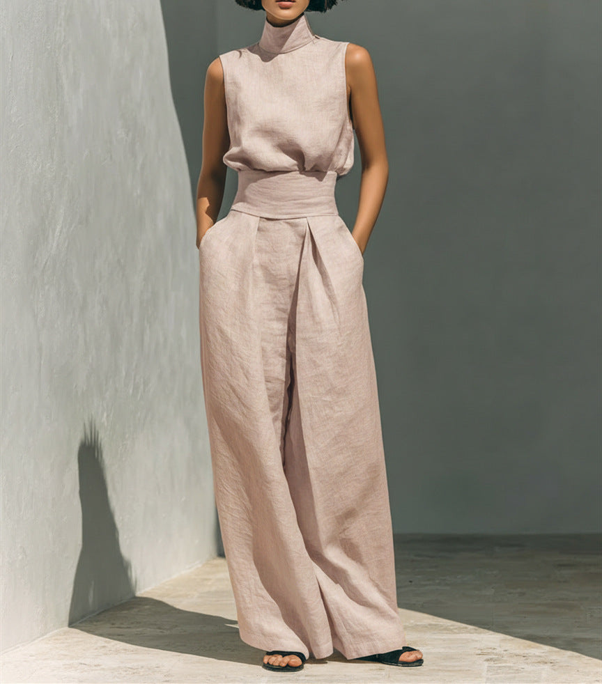Person wearing a light pink sleeveless top and wide-leg pants against a gray wall.