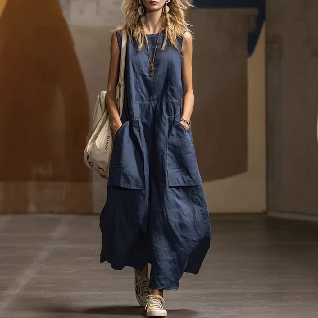 Woman wearing a blue dress with pockets, holding a beige bag, on a blurred street background.