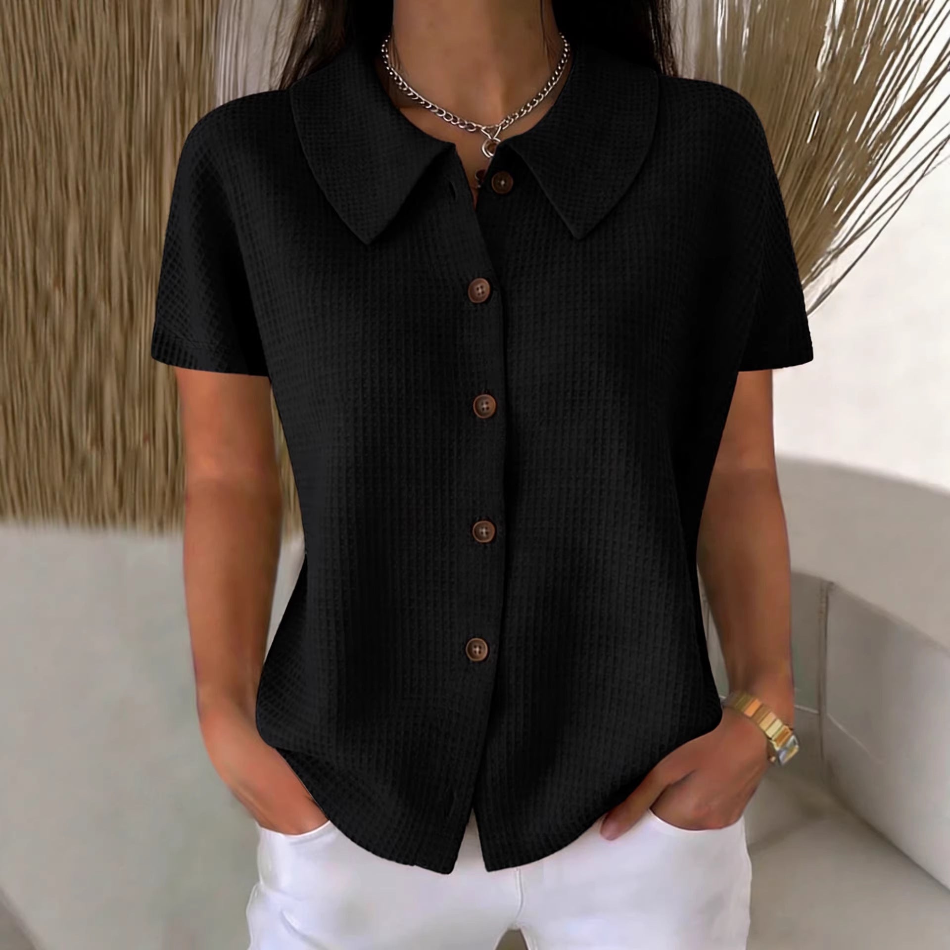 Person wearing a black short-sleeve button-up shirt with white pants against a neutral background