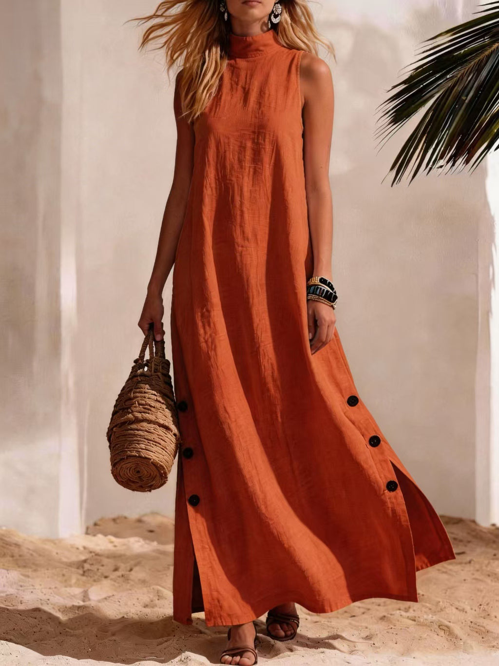 Woman in a long rust-colored dress with black buttons standing on sand with a blurred background