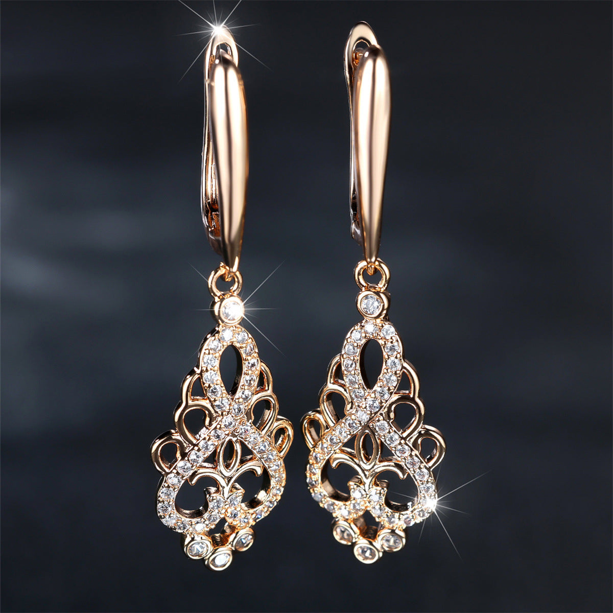 Rose gold earrings with intricate designs and sparkling stones on a dark background