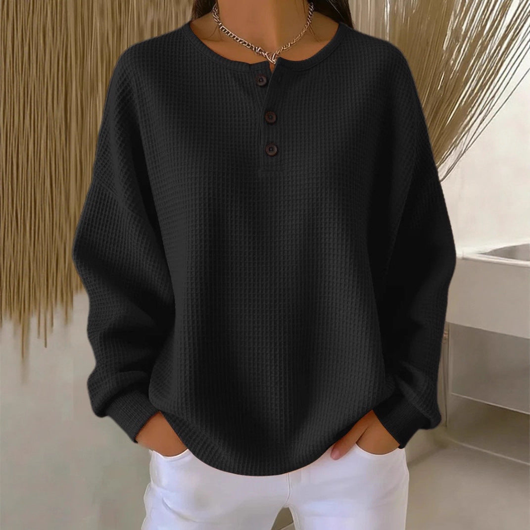 Person wearing a black ribbed sweater with buttons and white pants against a neutral background