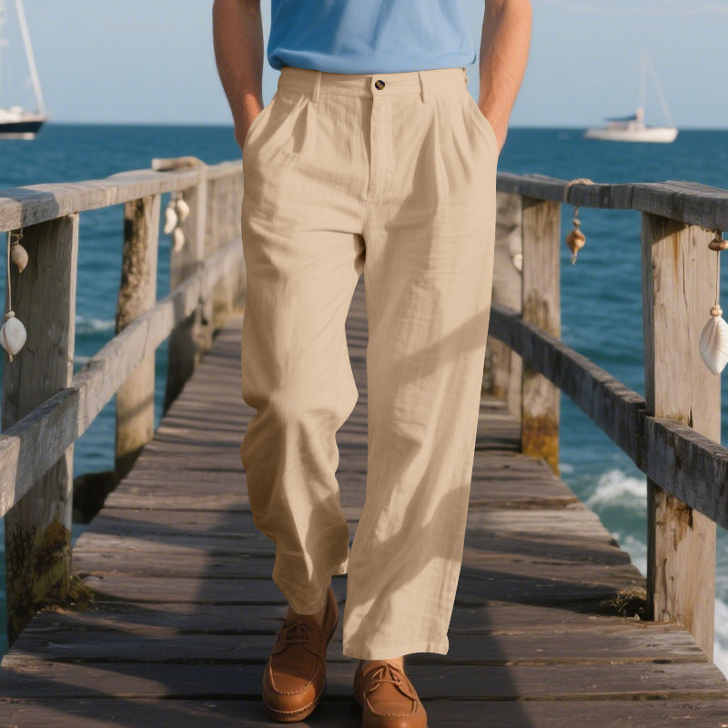 Person wearing beige pants standing on a wooden pier with ocean and sailboats in the background