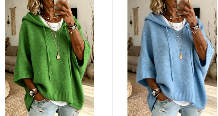 A side-by-side comparison of a women's oversized knit hoodie sweater shown in two colors: a vibrant green on the left and a light sky blue on the right. Both are modeled by a woman taking a mirror selfie in a cozy living room setting.