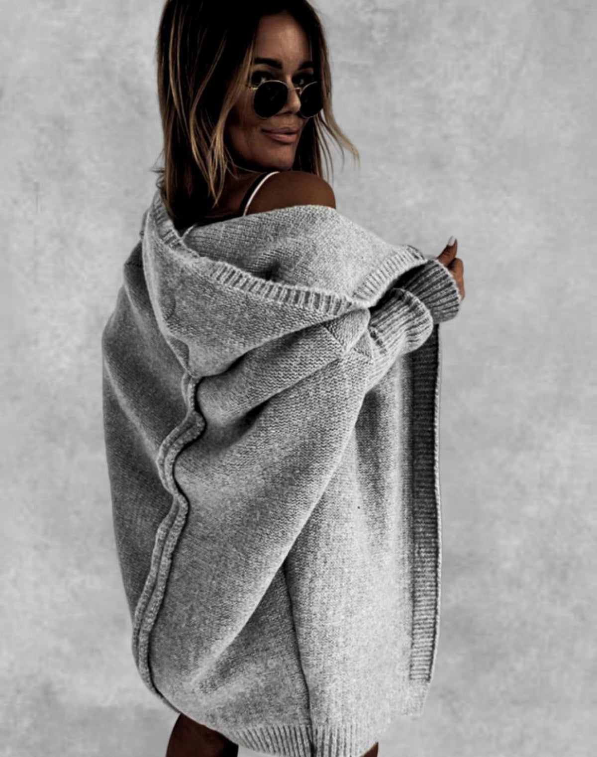 Woman wearing a gray knit poncho against a plain background