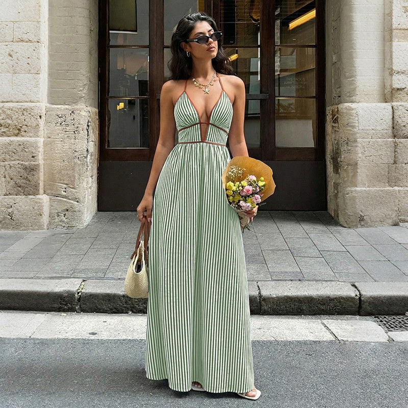 Woman in a red and white striped dress holding flowers and a yellow bag on a city street.