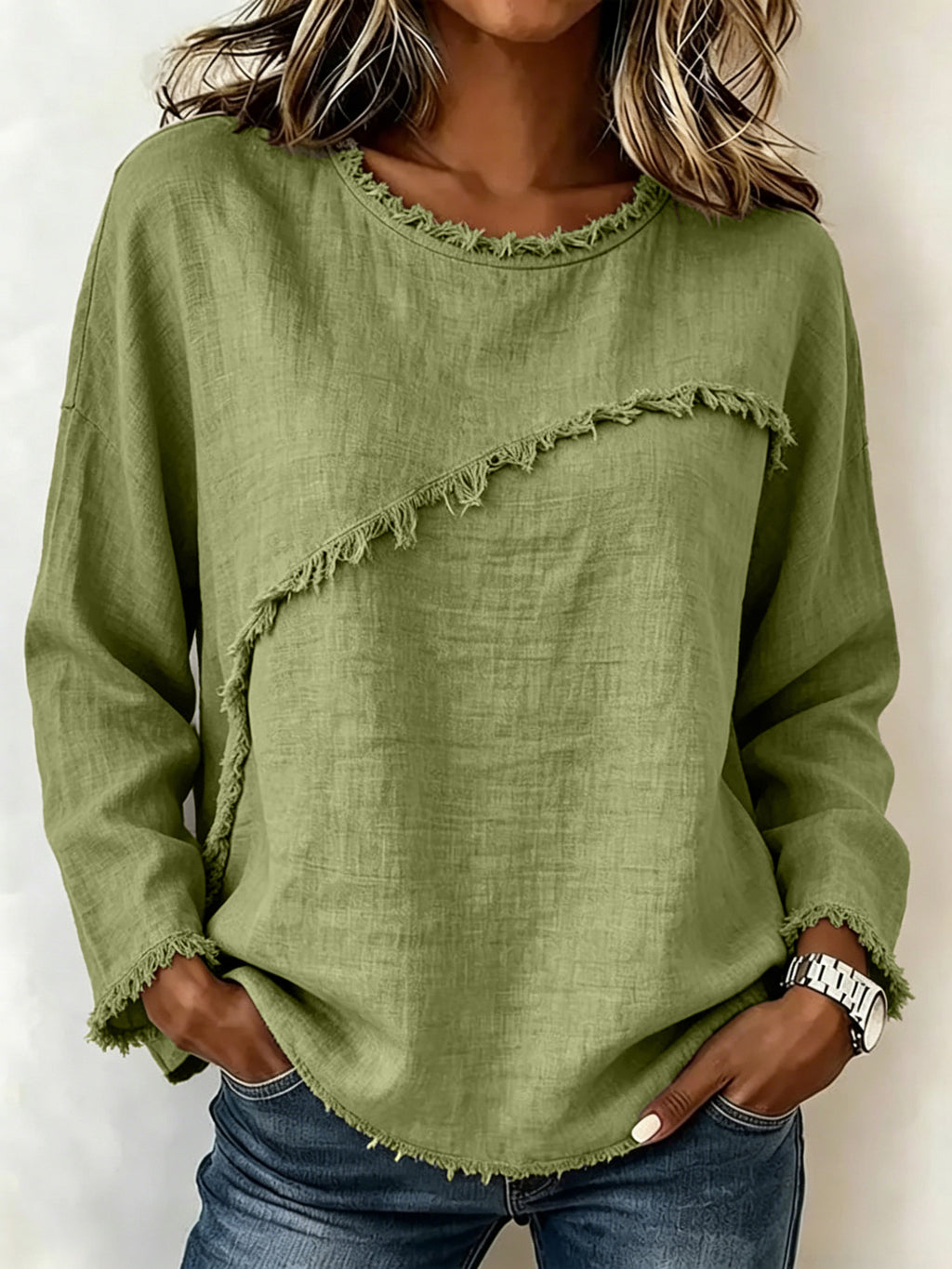 A woman wearing a sage green long-sleeve linen top with frayed trim details, paired with blue jeans.