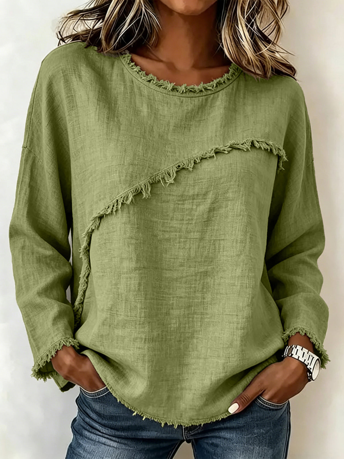 A woman wearing a sage green long-sleeve linen top with frayed trim details, paired with blue jeans.
