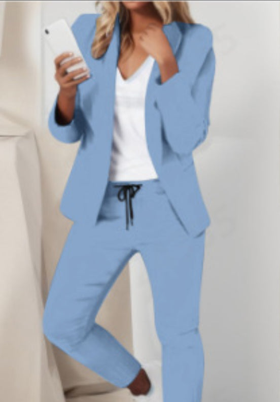 Woman wearing a light blue suit with a white top, holding a phone.
