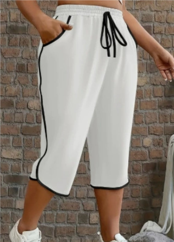 White capri pants with black trim worn by a person against a brick wall.