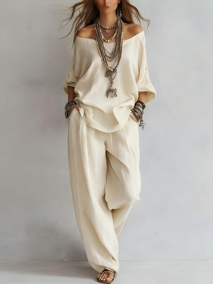 Person wearing a loose-fitting cream-colored outfit with layered necklaces on a plain background