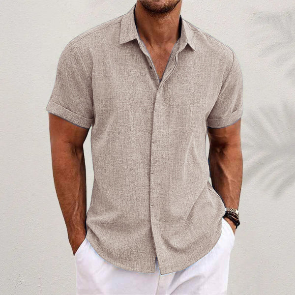 Man wearing a beige short-sleeve shirt and white pants against a light background