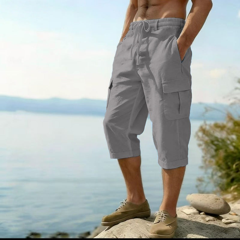 Person wearing gray cargo shorts standing by a body of water with mountains in the background.