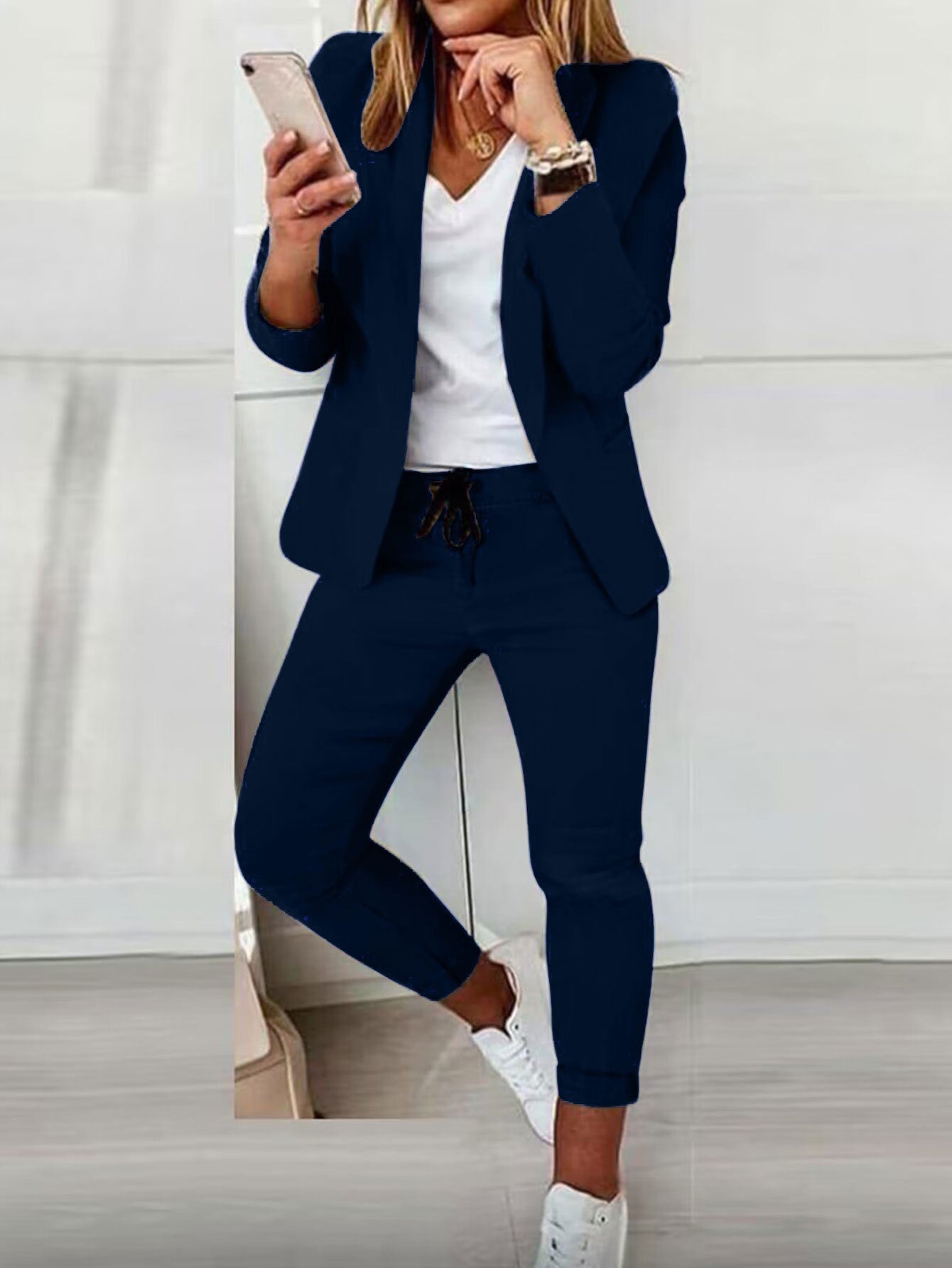 Person wearing a navy blue suit with white sneakers and holding a phone.