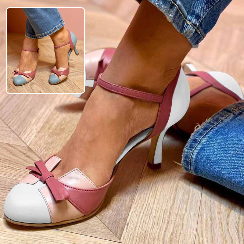 Close-up of a person wearing pink and white shoes with a bow detail on a wooden floor.