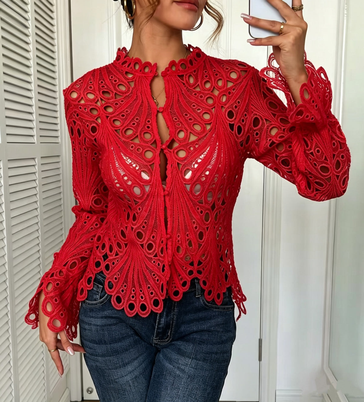 A woman takes a mirror selfie wearing a vibrant red, long-sleeved crochet lace top with intricate cutout patterns and blue jeans.
