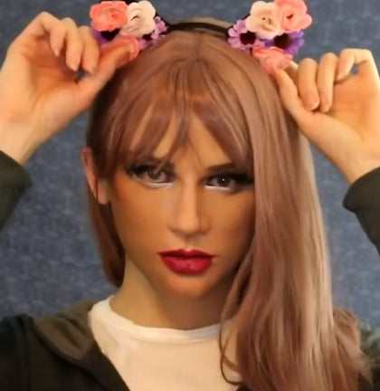 Person wearing a wig with floral headband against a blue background