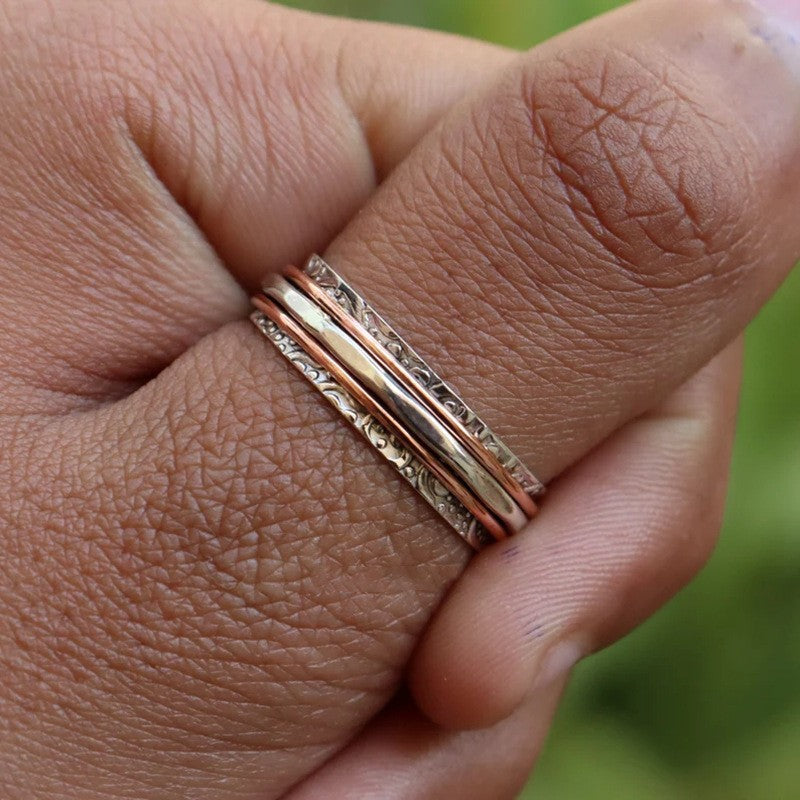 Close-up of a hand wearing two gold rings with a blurred green background