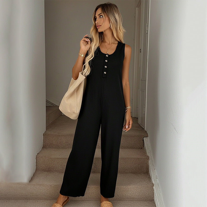 Woman in a black jumpsuit holding a beige bag on a staircase.