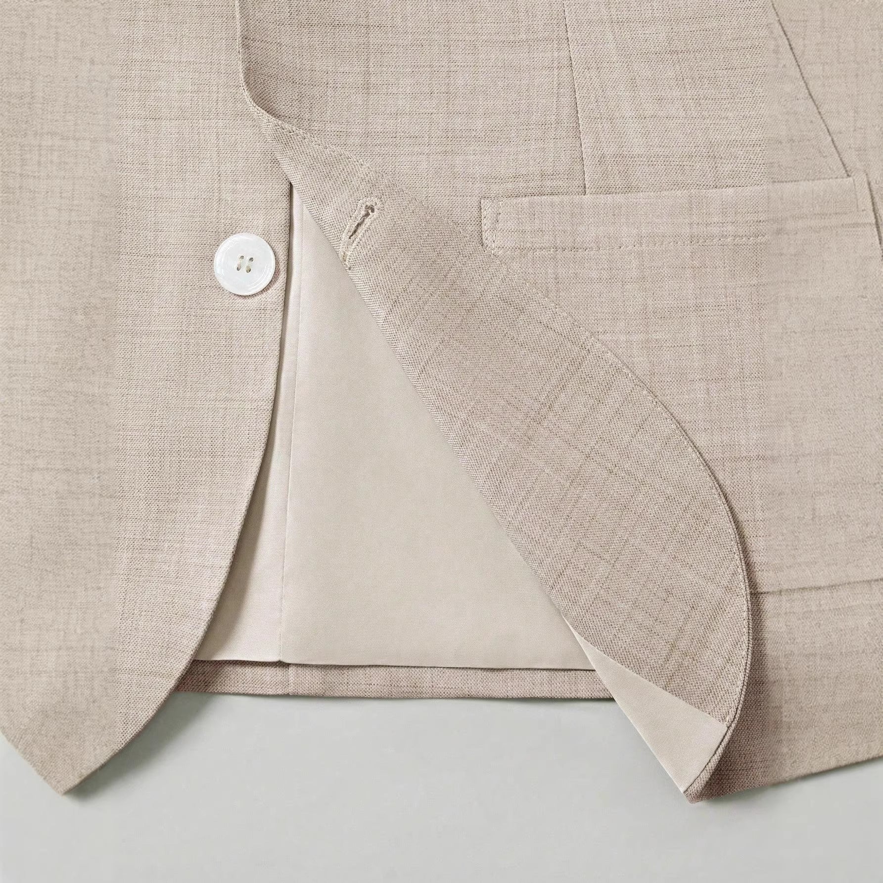 Close-up of a beige blazer with a button on a light gray background