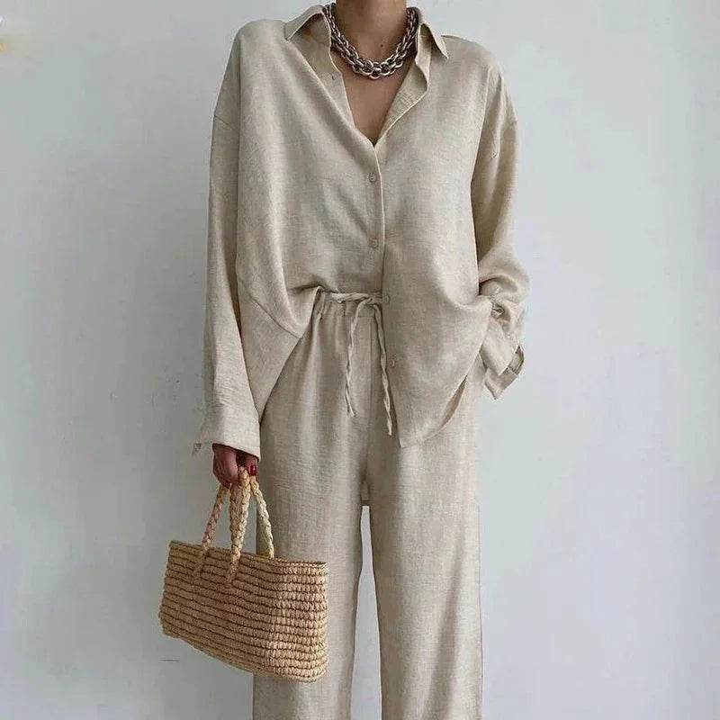 Woman in beige linen set with oversized shirt, drawstring pants, chain necklace, and straw bag