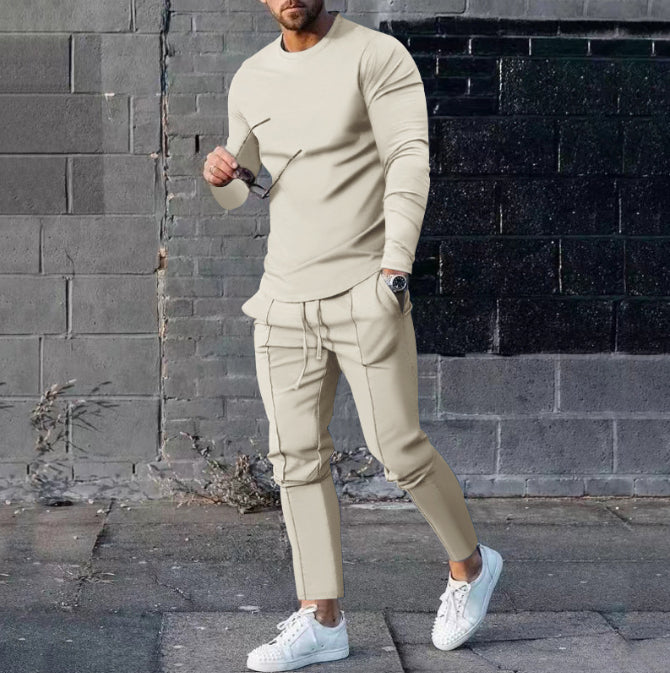 Man wearing a beige outfit with white sneakers against a brick wall.