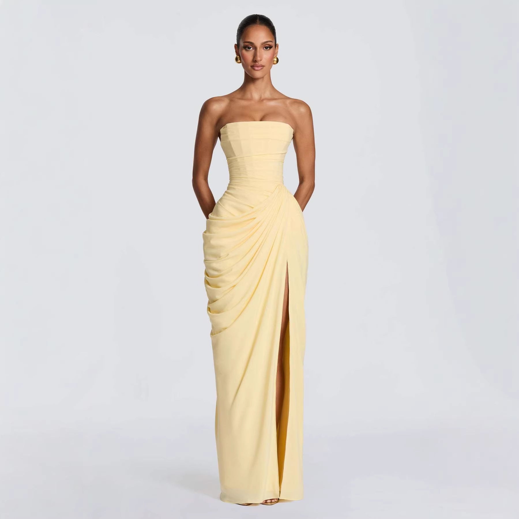 Woman wearing a strapless yellow gown with a slit on a light gray background