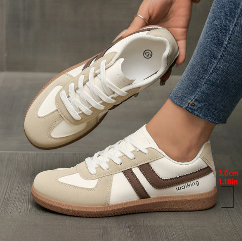 Beige and white sneakers with brown accents worn by a person on a gray surface.
