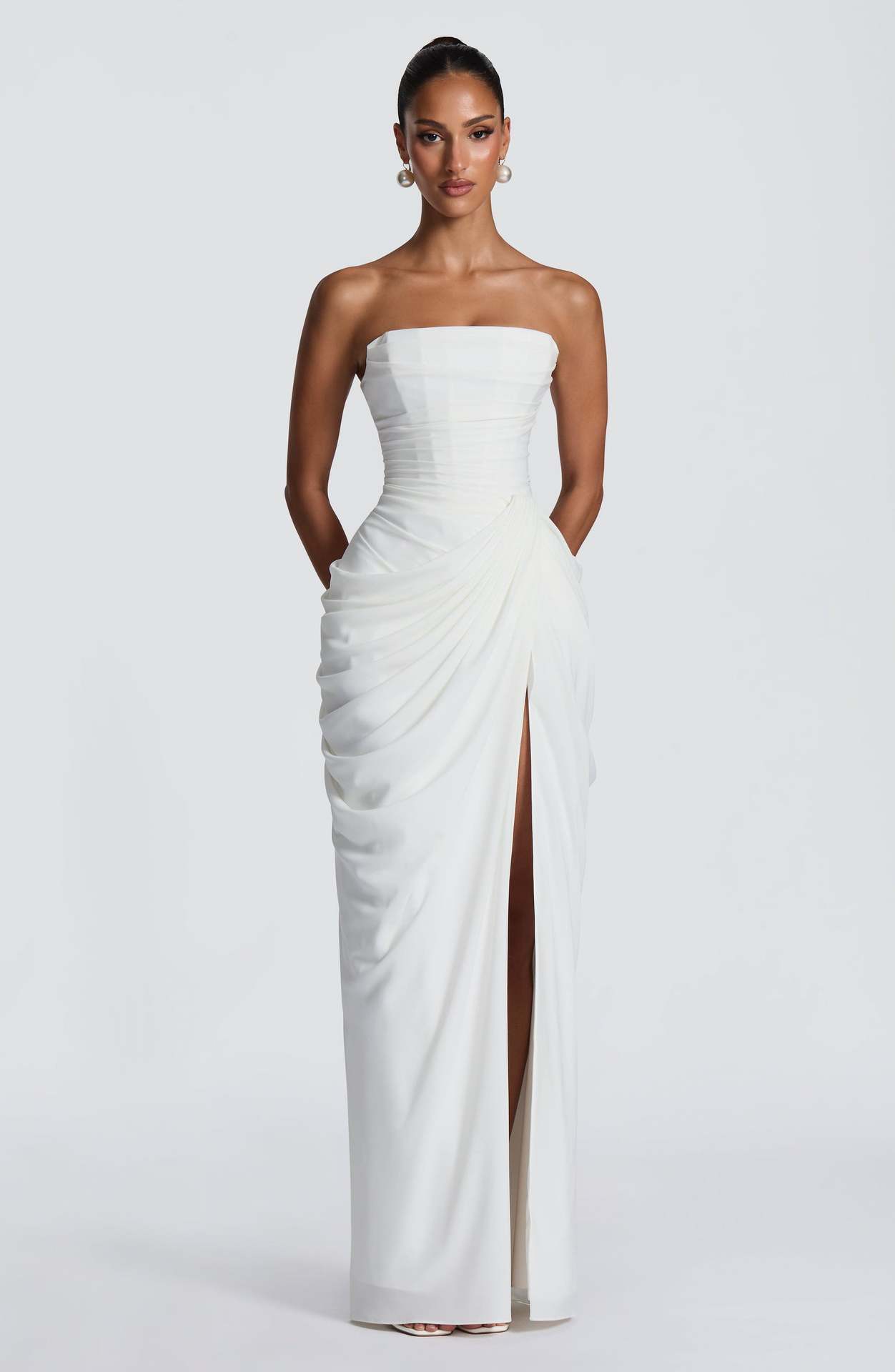 Woman wearing a strapless white gown with a slit on a white background