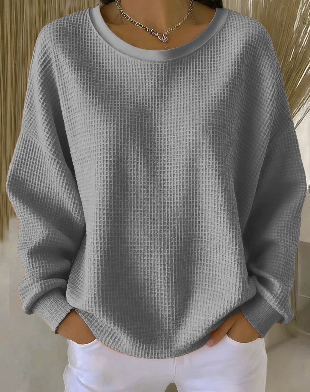 Person wearing a gray textured sweater with white pants against a neutral background