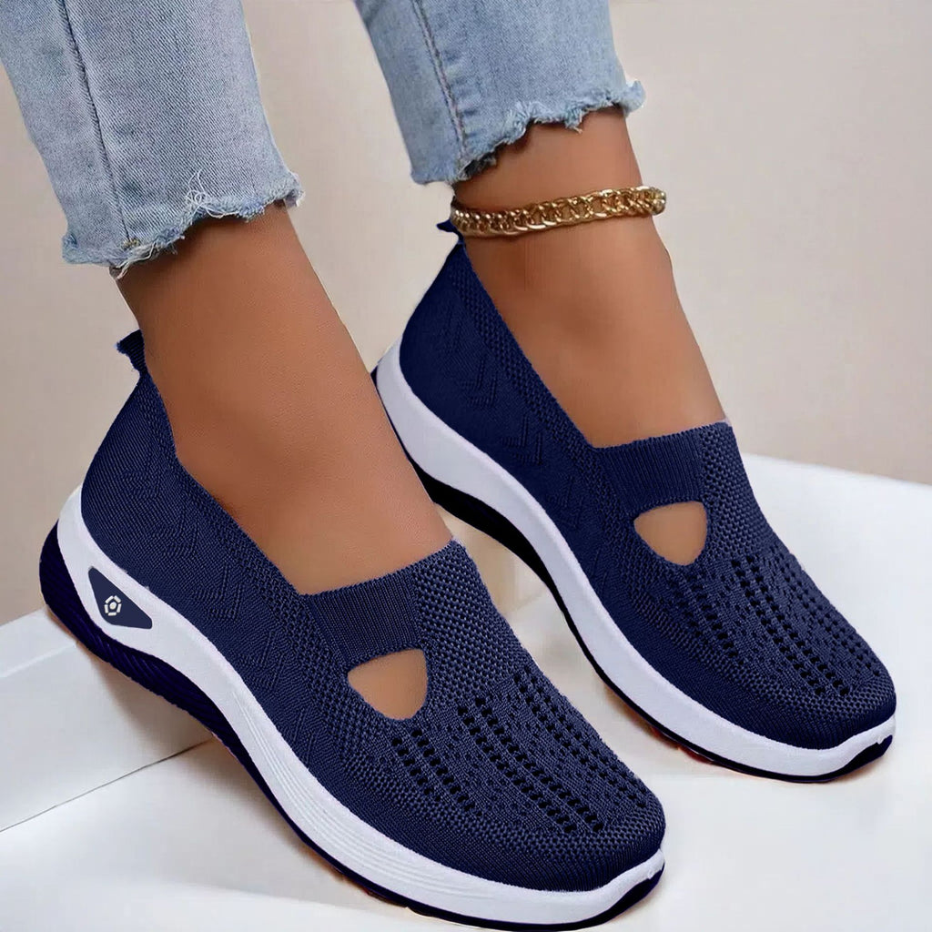 Navy blue slip-on shoes with white soles worn by a person on a light background