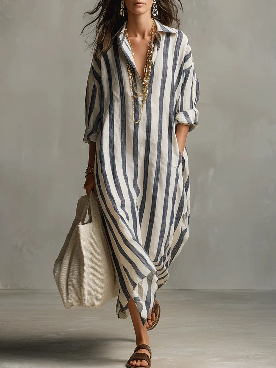 Woman wearing a long, striped dress holding a beige bag against a neutral background