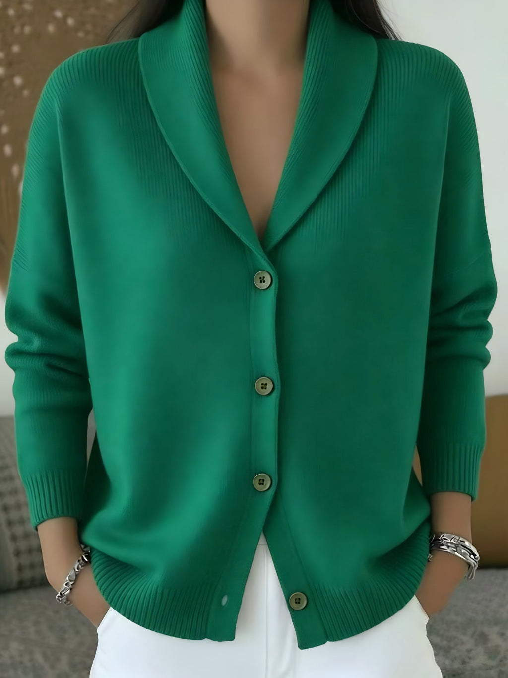 A woman wearing a vibrant green shawl-collar cardigan sweater with brown buttons, paired with white pants.