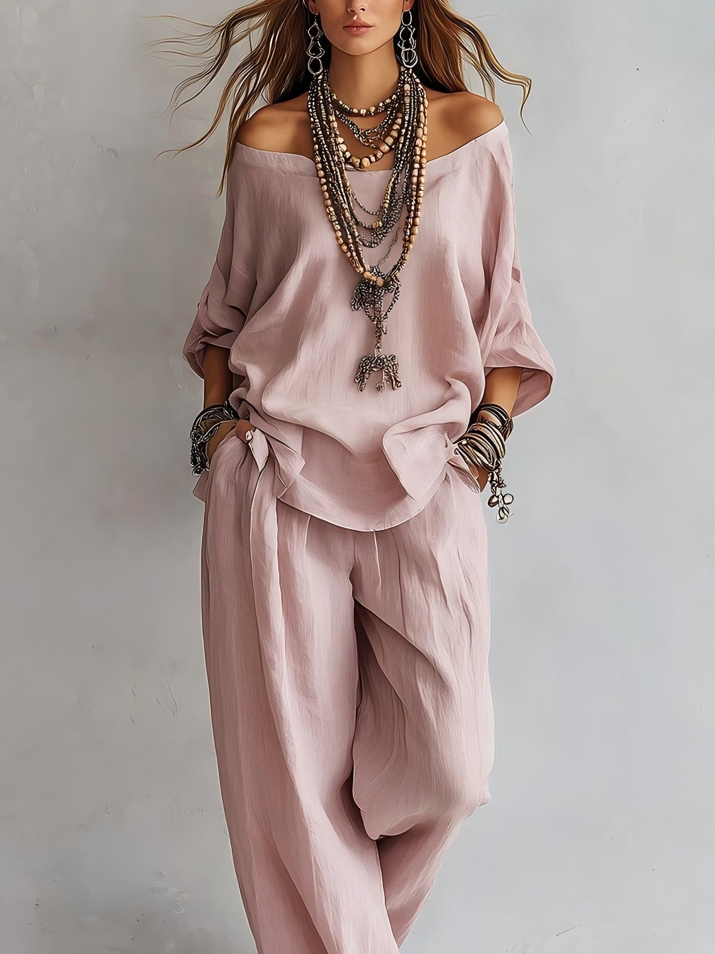 Person wearing a loose-fitting pink top and pants with layered necklaces and bracelets on a plain background