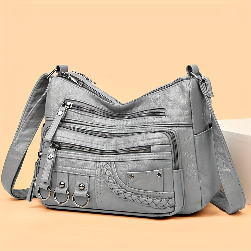 Gray leather handbag with multiple zippers on a beige background