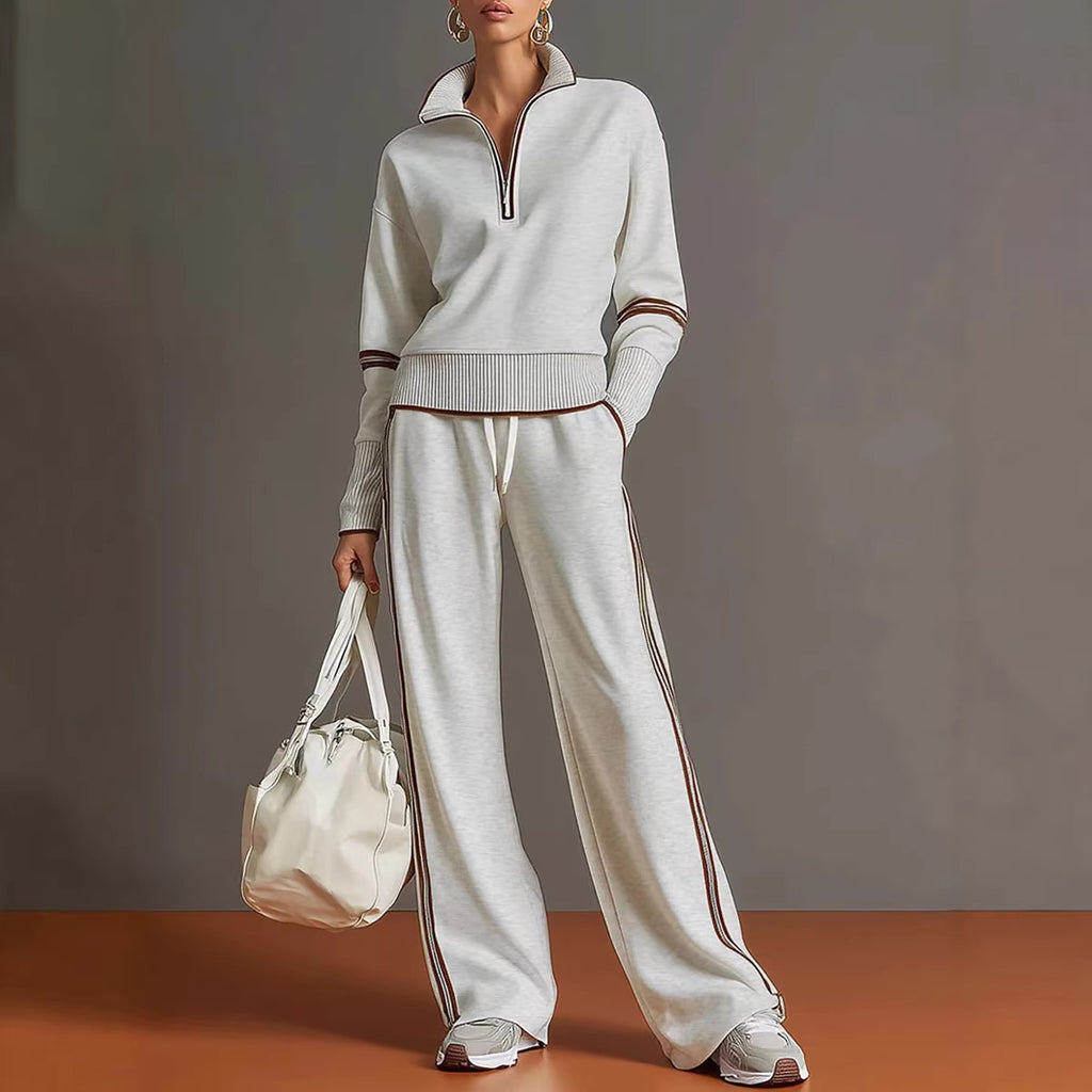 Person wearing a white tracksuit with brown accents, holding a matching bag against a neutral background.