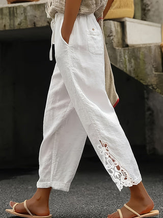 Person wearing white pants with lace details and brown sandals on a blurred background