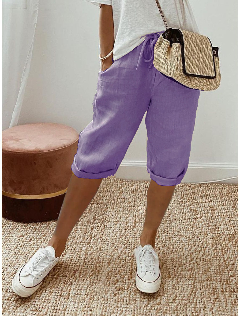 Person wearing purple shorts, white sneakers, and a straw bag indoors.