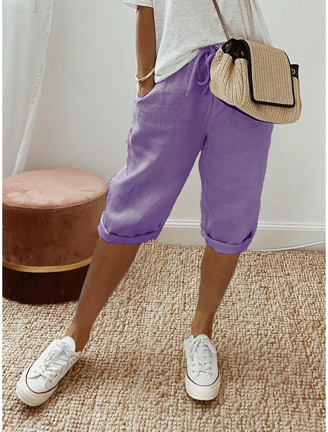 Person wearing purple shorts, white sneakers, and a straw bag indoors.