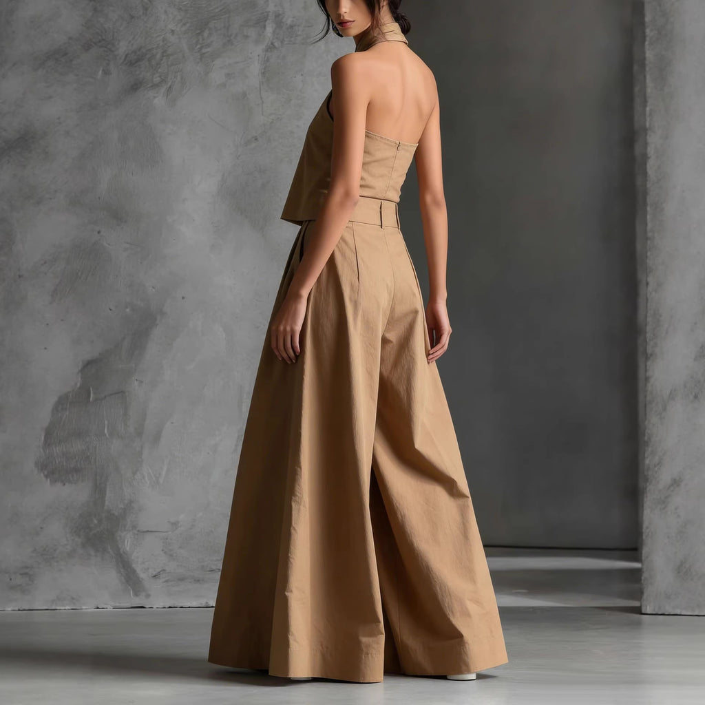 Woman wearing a beige halter neck jumpsuit against a gray concrete wall.
