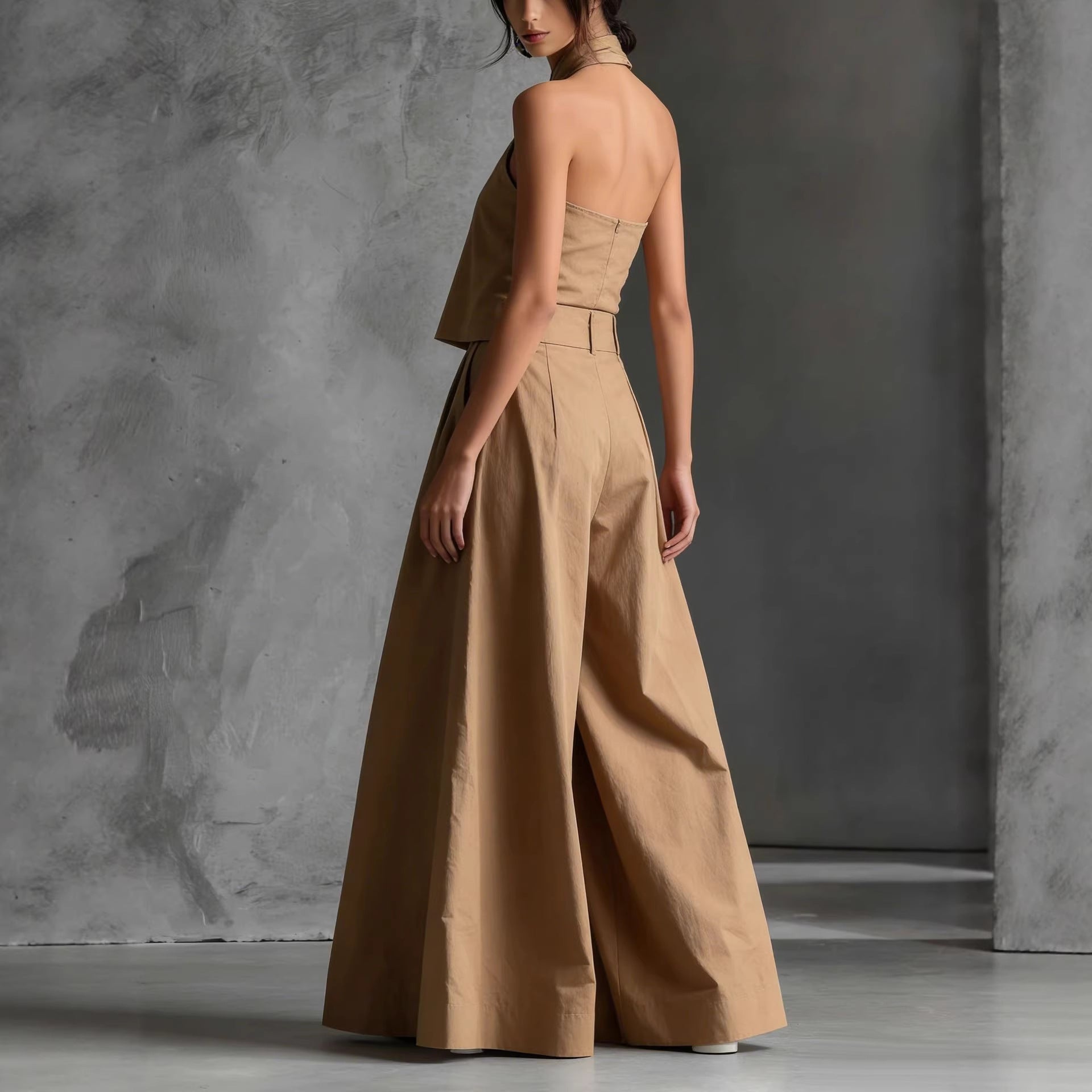 Woman wearing a beige halter neck jumpsuit against a gray concrete wall.
