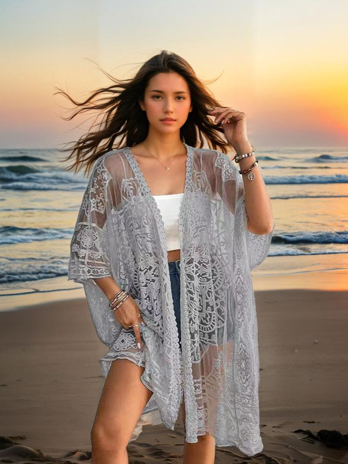 Woman in a lace cover-up standing on a beach at sunset