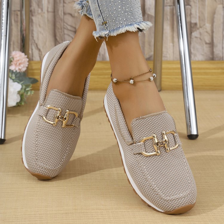 Beige loafers with gold buckles worn by a person on a wooden floor.